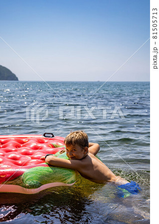Funny kid boy floating on inflatable rubber strawberry lifebuoy surrounded by pure clear sea water Funny kid boy floating on inflatable rubber strawberry lifebuoy surrounded by pure clear sea water 81505713