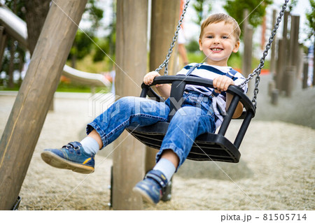 Smiling boy riding on swing at amusement forest park or childish playground having positive emotion Smiling boy riding on swing at amusement forest park or childish playground having positive emotion 81505714
