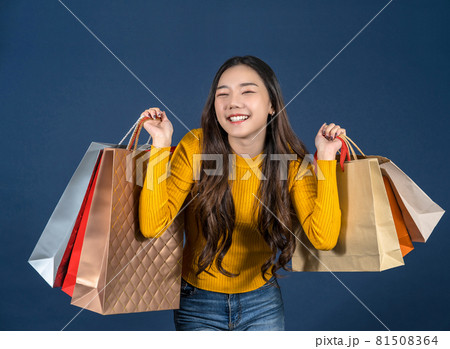 Happy young Asian smiling young woman Carrying a shopping coloful bag on classic blue color background, exciting for sales discount, black friday and consumerism concept, summer fashion, Full body. 81508364