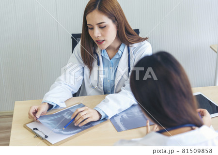 Two asian women doctors discuss meeting doctor's office medical clinic looking x-ray film consulting patient disease. Asian medical lab young women talking together discussing healthcare teamwork 81509858