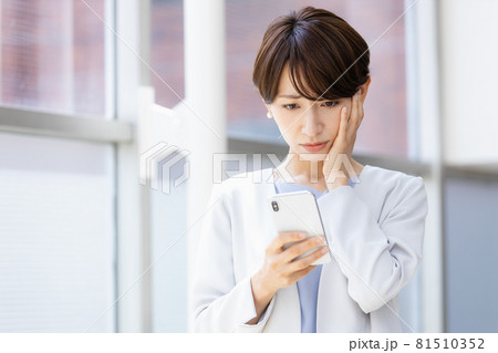 手に持ったスマホを見てネガティブな表情を見せる女性 81510352