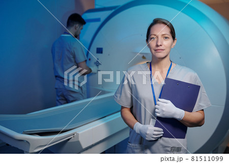 Young nurse in uniform and gloves standing in front of medical machine 81511099