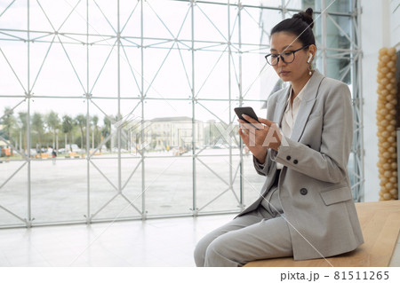 Young serious businesswoman with earphones watching video in smartphone 81511265