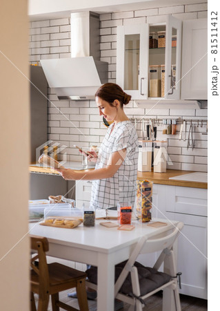 Happy female housewife smiling posing and takes pictures of the barcode at modern Nordic style kitchen food storage organization 81511412