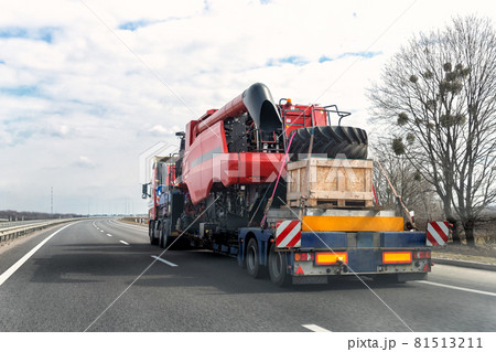 Heavy industrial truck with semi trailer platform transport disassembled combine harvester machine on common public highway road on sunset sunrise day. Agricultural equipment transportation service 81513211