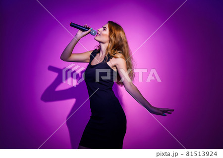 Photo portrait of woman holding microphone in hands isolated on pastel pink colored background 81513924