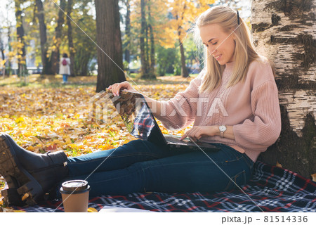 A young woman works in a park, typing on a laptop 81514336