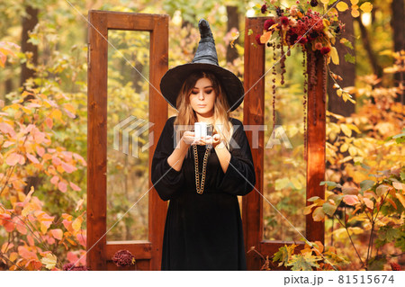 Young woman in Witch costum and hat with candle in hands stands against autumn forest background Young woman in Witch costum and hat with candle in hands stands against autumn forest background 81515674