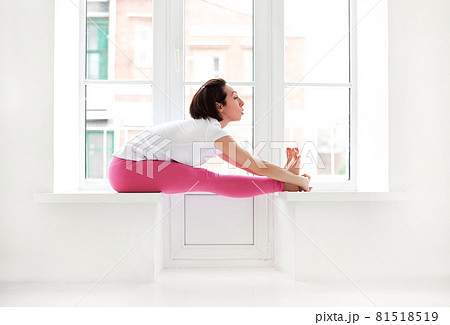 Young slender fit woman in pink long bodysuit performing yoga pose, isolated over white studio background 81518519
