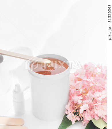 depilation sugaring wax in white container with spatula and strips fo hair removing. skin care, smooth skin treatment. home depilation set. sugaring paste flows down to a jar depilation sugaring wax in white container with spatula and strips fo hair removing. skin care, smooth skin treatment. home depilation set. sugaring paste flows down to a jar 81520543