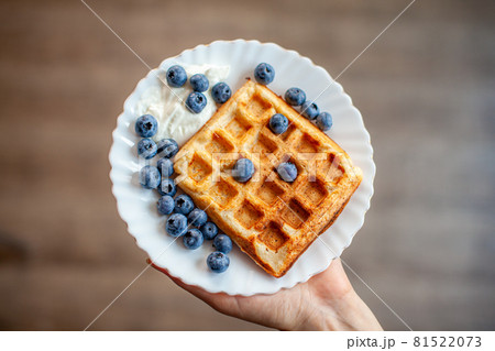 A woman holds in her hand a plate on which fresh waffles with berries are ready. Homemade waffles with strawberries and blueberries. Delicious Breakfast with berries. A woman holds in her hand a plate on which fresh waffles with berries are ready. Homemade waffles with strawberries and blueberries. Delicious Breakfast with berries. 81522073