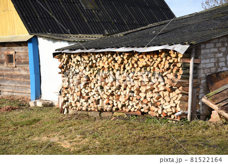Chopped logs of firewood piled under the roof in the village in a backyard. Chopped logs of firewood piled under the roof in the village in a backyard. 81522164