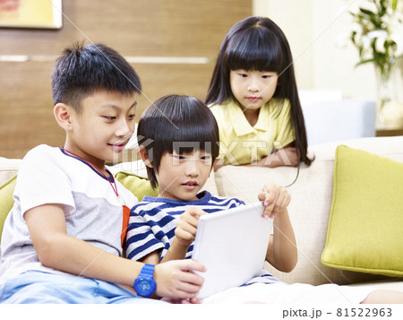 three asian children sitting on couch at home playing video game using digital tablet 81522963