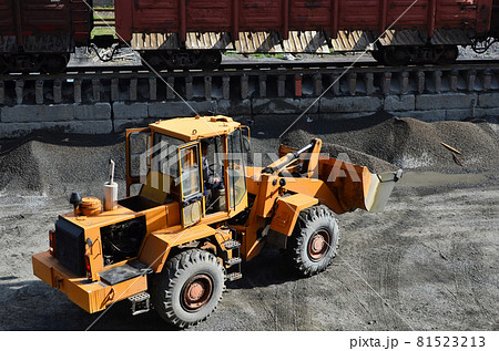 Wheel loader unloading bulk cargo from freight cars at a cargo railway station. Wheel loader unloading bulk cargo from freight cars at a cargo railway station. 81523213