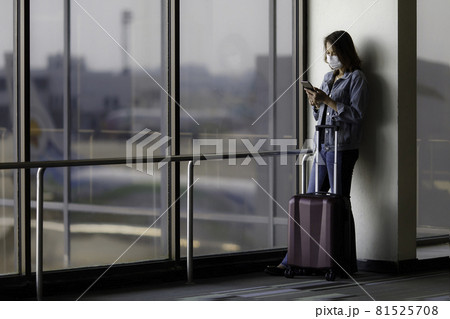 Beautiful Asian traveler wearing hygiene protective mask standing alone and using a smartphone at the airport while waiting for a flight. Idea for traveling in a new normal situation Beautiful Asian traveler wearing hygiene protective mask standing alone and using a smartphone at the airport while waiting for a flight. Idea for traveling in a new normal situation 81525708
