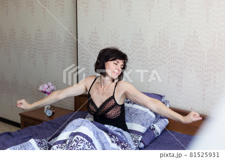 The brunette is sitting on the bed in the early morning stretching and basking in bed trying to wake up The brunette is sitting on the bed in the early morning stretching and basking in bed trying to wake up 81525931