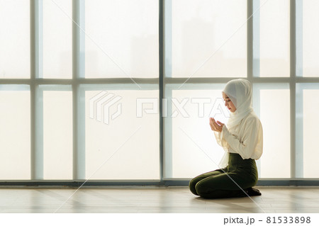 Young and beautiful Asian Muslim woman sitting on floor and praying with respect and calm manner Young and beautiful Asian Muslim woman sitting on floor and praying with respect and calm manner 81533898