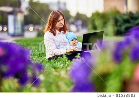 Woman makes remote work with baby on knees in city garden. Woman makes remote work with baby on knees in city garden. 81533983