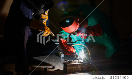 mechanics workers work overtime hardly at night in a factory. Engineers wearing safety outfits with mechanic jumpsuits, gloves, boots, and welding helmets working on metal welding 81534409