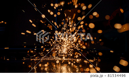 spark in a dark background from a hot red metal cut by a steel cutting machine in a factory. Nice bokeh in warm black background. Flashes from cutting iron 81534496
