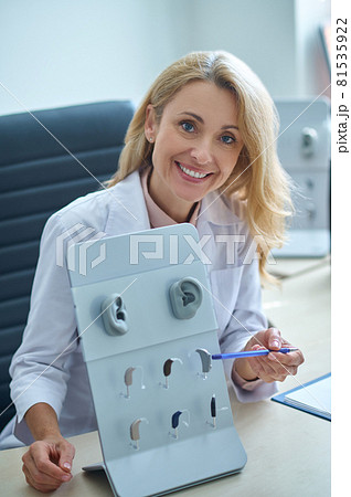Cheerful otorhinolaryngologist pointing with a pen at listening apparatuses 81535922
