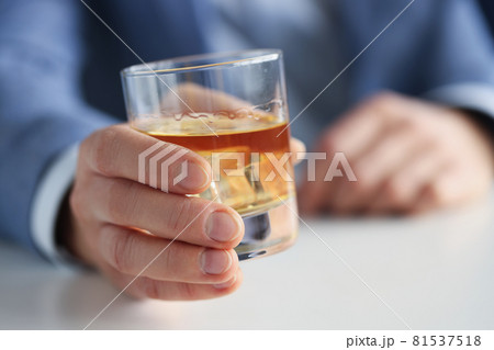 Man in suit holding glass of whiskey with ice in his hand closeup 81537518