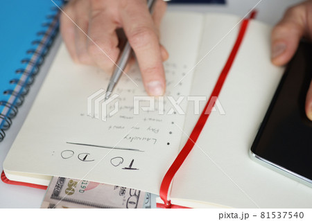 Man holding notepad with to-do list for today near mobile phone closeup Man holding notepad with to-do list for today near mobile phone closeup 81537540