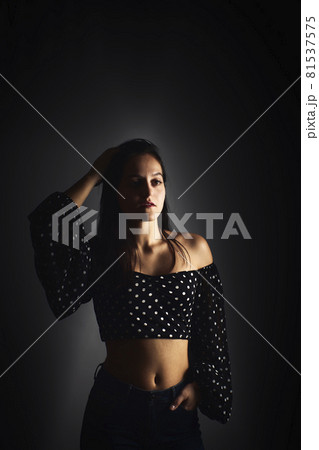 Half-length portrait of a young girl with a smile looking towards the camera, on a dark studio background 81537575