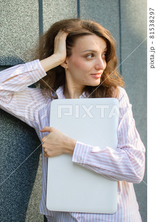 Female portrait of young woman with silver laptop, businesswoman is posing with digital tablet outside on dark wall background while waiting for a meeting during a break from work 81538297