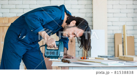 Good looking Asian carpenter wearing coverall dress working for DIY jobs in carpenter room with several kinds of woods and types of equipment 81538838