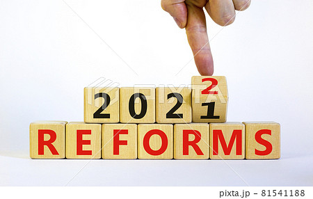 Symbol of planning 2022 reforms new year. Businessman turns a wooden cube and changes words 'reforms 2021' to 'reforms 2022'. Beautiful white background, copy space. Business, 2022 reforms concept. Symbol of planning 2022 reforms new year. Businessman turns a wooden cube and changes words 'reforms 2021' to 'reforms 2022'. Beautiful white background, copy space. Business, 2022 reforms concept. 81541188