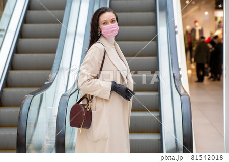 middle aged woman with gloves and mask on escalator in public place 81542018