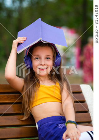Preteen school girl with book on bench in park Preteen school girl with book on bench in park 81542019