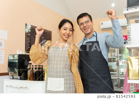 Cheerful business owners standing welcomingly together in front of the counter of their cafe. 81542593
