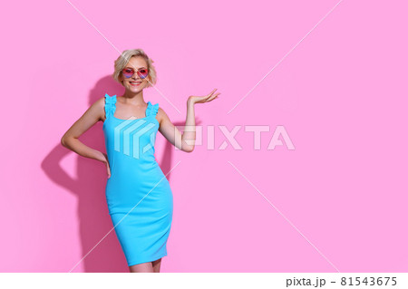 Portrait of beautiful blonde woman in blue dress with sunglasses posing on pink studio background Portrait of beautiful blonde woman in blue dress with sunglasses posing on pink studio background 81543675