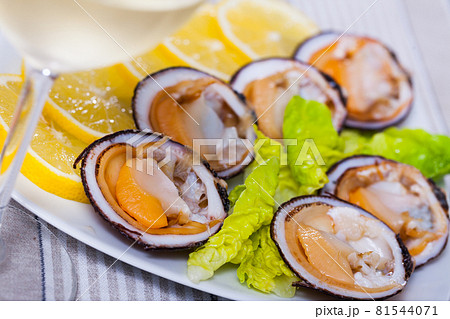 Tasty raw dog cockle, lemon and greens at plate and glass of wine 81544071