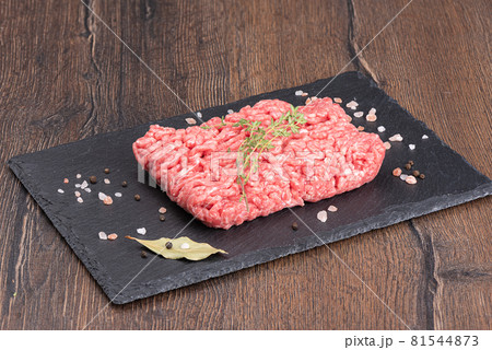 Ground beef with thyme and spices on a stone board over a wooden background. Ground beef with thyme and spices on a stone board over a wooden background. 81544873