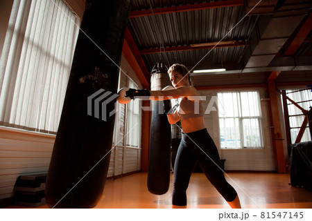 Young woman doing boxing workout in the gym, she is wearing boxing gloves and punching a punching Young woman doing boxing workout in the gym, she is wearing boxing gloves and punching a punching 81547145
