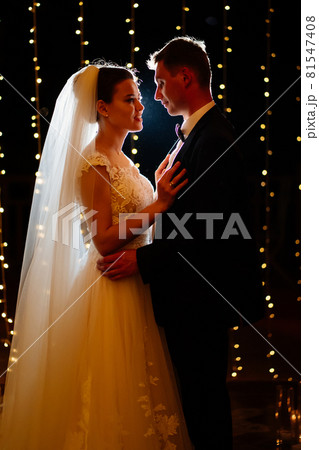 bride and groom at evening wedding ceremony in park among light bulbs 81547408