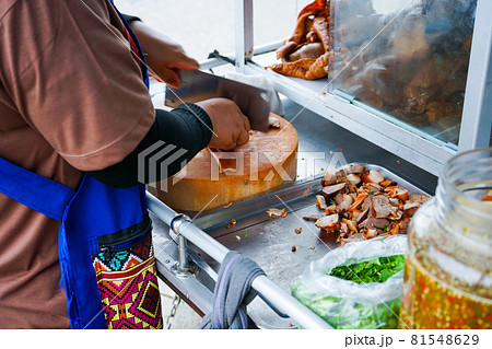 Delicious stewed ear pork at the street food. Motion blurred hand of seller chops the pork on cutting board. Delicious stewed ear pork at the street food. Motion blurred hand of seller chops the pork on cutting board. 81548629