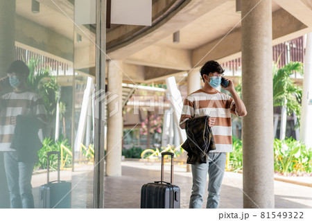 Travel. A man wearing glasses with a striped shirt and mask is talking on a mobile phone. carries jacket on the right hand and luggage is placed on the right Travel. A man wearing glasses with a striped shirt and mask is talking on a mobile phone. carries jacket on the right hand and luggage is placed on the right 81549322