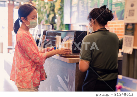Asian Woman customer in protective mask receive drink from waiter on coffee bar counter. 81549612
