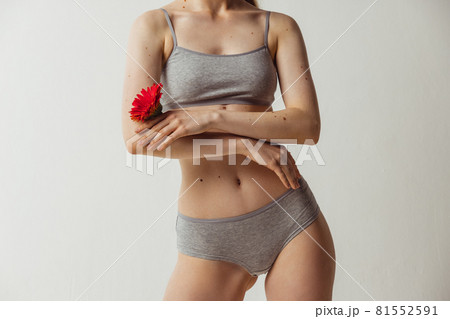 Cropped shot of young attractive woman holding flower as symbol of tenderness isolated over gray studio background. Natural beauty, authenticity concept. 81552591