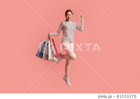Big Sales Concept. Happy Asian Female Jumping With Shopping Bags And Showing Ok Gesture, Excited Young Korean Woman Enjoying Seasonal Discounts, Posing Isolated Over Pink Background, Copy Space 81553370