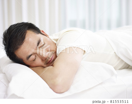 asian man lying on front in bed sleeping 81553511