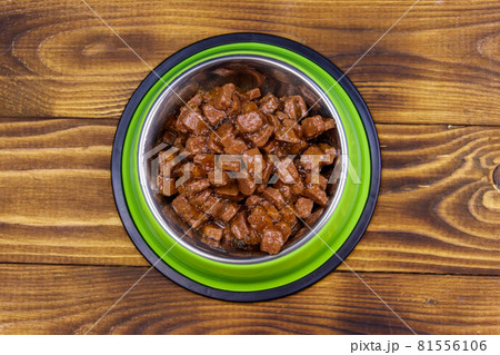 Canned food for cats or dogs in green metal bowl on wooden floor. Top view 81556106