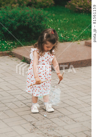 A cheerful girl catches soap bubbles with her hands and laughs. Happy childhood, summer time. Portrait of young toddler girl 81561159