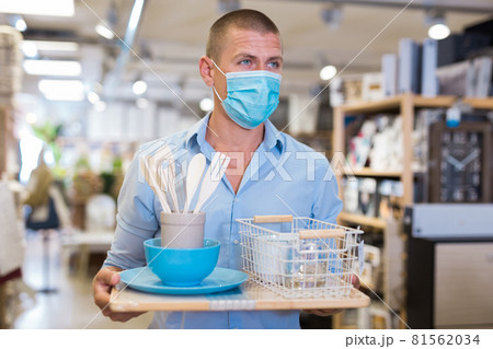 Customer in protective mask holding purchases and walking in household goods store Customer in protective mask holding purchases and walking in household goods store 81562034