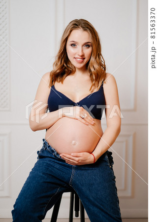 an attractive pregnant woman with a bare tummy sits on a chair. an attractive pregnant woman with a bare tummy sits on a chair. 81563370