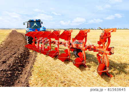 Agricultural tractor coupled to a metal plow on a harvested wheat field. 81563645